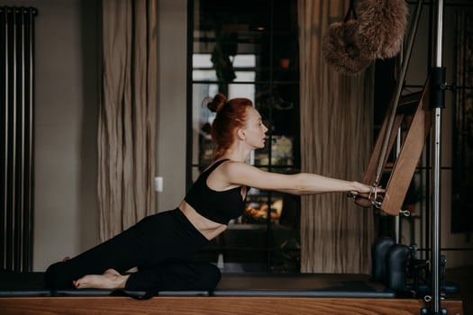 Sportive ginger woman stretching athletic body on cadillac reformer during pilates training photo