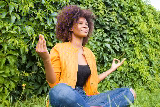 A happy and young African American woman meditates on the grass photo