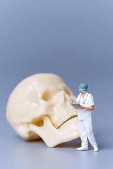 Miniature people Doctor with a giant human skull on a grey background photo