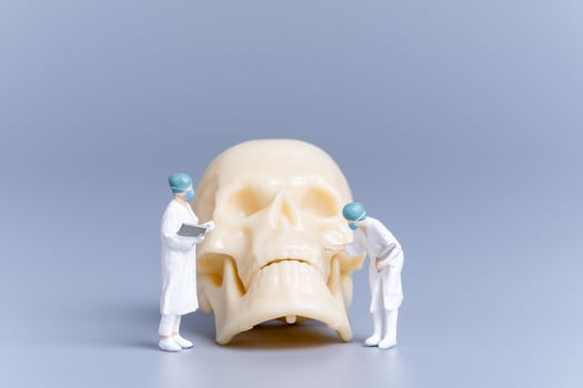Miniature people Doctor with a giant human skull on a grey background photo