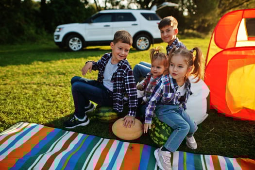 Four kids spending time together. Outdoor picnic blanket, sitting with watermelons. photo