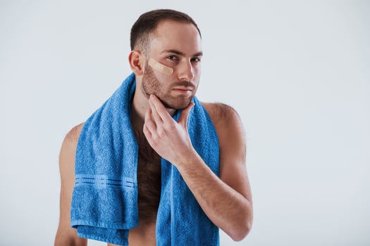 Looking in the mirror. Man with blue towel stands against white background in the studio photo