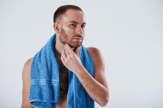 Modern skin care. Man with blue towel stands against white background in the studio photo