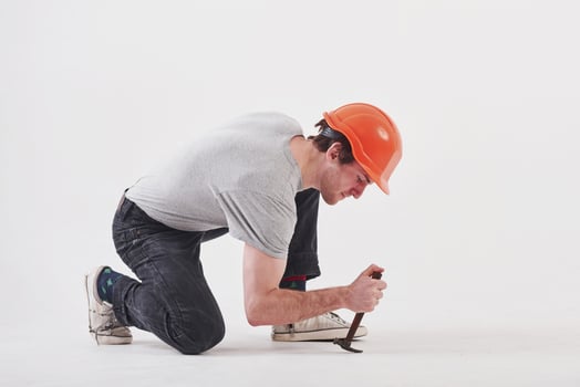 Man in casual clothes and orange colored hard hat have some work using hammer. White background photo
