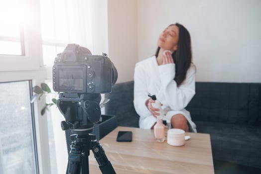Backstage of the photoshoot. In front of camera on the tripod. Conception of fashion and skincare. Brunette girl uses cosmetics photo