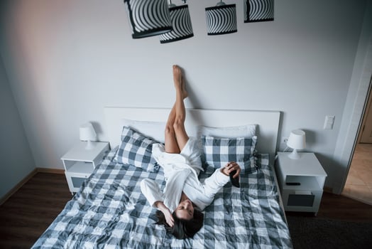 Upside down. Beautiful girl in white robe lying on the bed at morning time and using smartphone photo