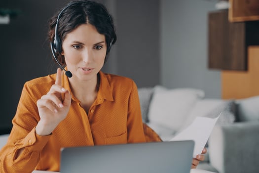 Young Spanish woman tutor wearing headset looking at laptop screen during online class photo