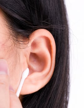 Woman with black hairs is cleaning her ears with white cotton bud. Personal hygiene concept. photo