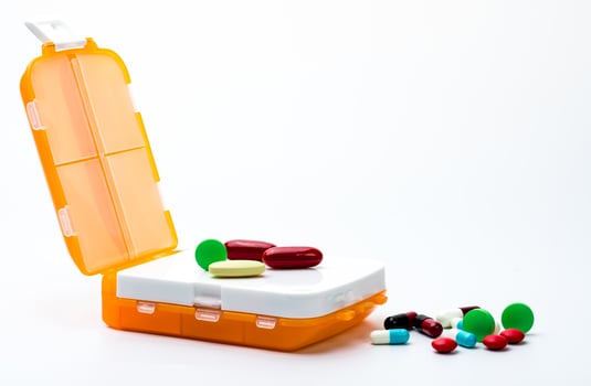 Orange pills box with colorful capsule pills isolated on white background with copy space. Prepare medicine before work or travel abroad concept. photo