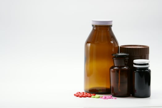 Pink, green, and red tablets on white background with amber drug bottle container. Light resistant packaging. Pharmaceutical industry. Vitamin and supplement product. Colorful pills and medicine jars. photo
