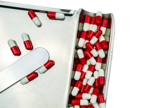 Top view of red-white antibiotic capsule pills on stainless steel drug tray. Antibiotc drug resistance. Prescription drugs. Pharmaceutical industry. photo