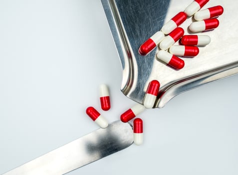 Red-white antibiotic capsule pills on stainless steel drug tray. Antibiotc drug resistance. Prescription drugs. Pharmaceutical industry. photo
