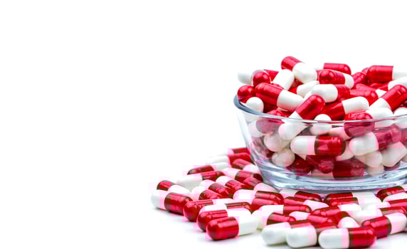 Red, white antibiotic capsules pills in glass bowl and some on white background with copy space. Drug resistance concept. Antibiotics drug use with reasonable and global healthcare concept. photo