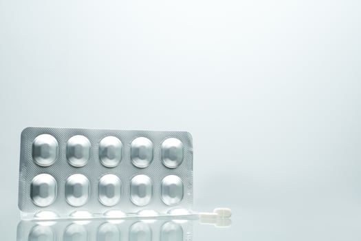 Silver aluminium foil blister pack of pills with 2 white tablet pills on white background with shadows and copy space for text. Pharmaceutical packaging and medicine storage concept photo