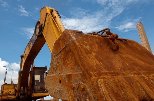 Closeup rusty metal bucket of old backhoe parked at construction site against blue sky. Excavating machine. Earth moving machine. Excavation vehicle. Dirt bucket of old digger. Construction industry. photo