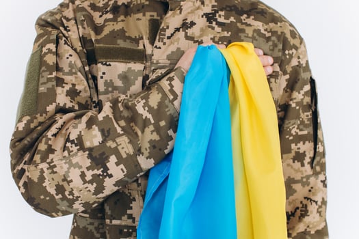 Ukrainian patriot soldier in military uniform holds a hand on a heart with a yellow and blue flag on a white background photo