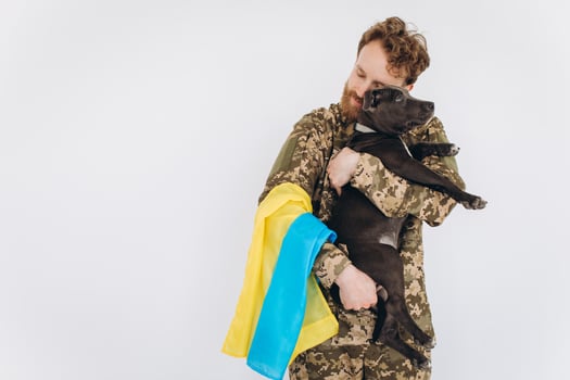 Ukrainian soldier in military uniform with a yellow and blue flag holds a dog in his arms on a white background photo