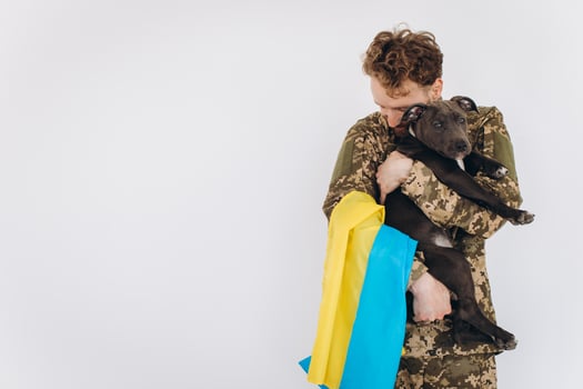 Ukrainian soldier in military uniform with a yellow and blue flag holds a dog in his arms on a white background photo