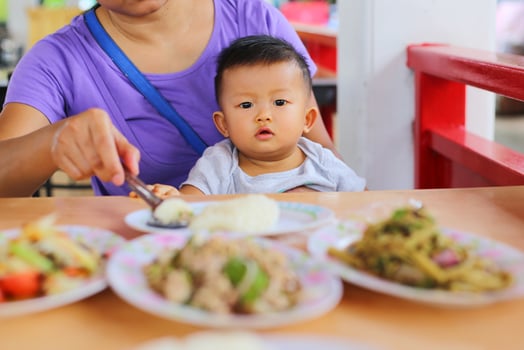 Mother feeding food to her son during lunch at restaurant. Asian baby eating with mother. photo