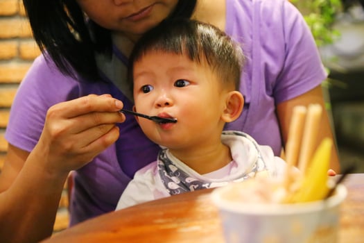 Mother feeding food to her son during dinner at restaurant. Asian baby eating with mother. photo