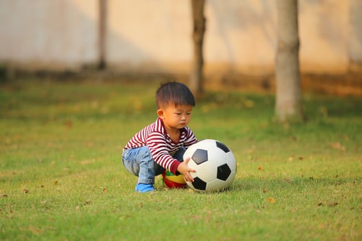 Asian boy playing football at the park. Kid with ball toy in grass field. photo