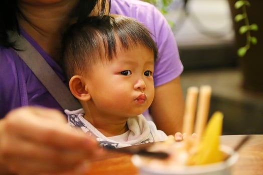 Mother feeding food to her son during dinner at restaurant. Asian baby eating with mother. photo