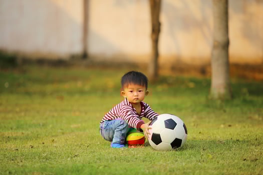 Asian boy playing football at the park. Kid with ball toy in grass field. photo
