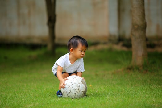 Asian boy playing football at the park. Kid with ball in grass field. photo