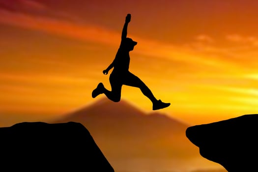 Silhouette of an athlete jumping on a rocky cliff photo