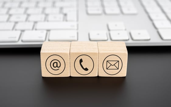 Contact us icons on wooden blocks and computer keyboard on black desk photo