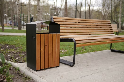 Wooden bench and trash can in the spring park against the background of trees. photo