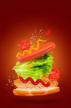 Flying ingredients for delicious hot dog on red background. Levitating sausage, tomatoes and lettuce. photo