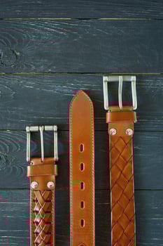 three leather brown belts on dark wooden background photo