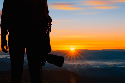 Young hipster photographer holding the camera with sunset on mountain natural background. photo