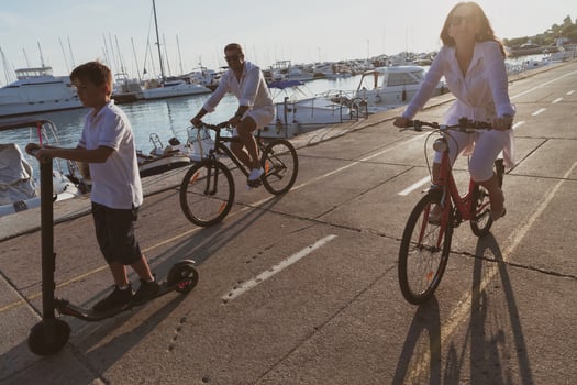 Happy family enjoying a beautiful morning by the sea together, parents riding a bike and their son riding an electric scooter. Selective focus photo