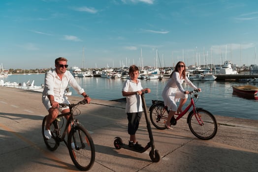 Happy family enjoying a beautiful morning by the sea together, parents riding a bike and their son riding an electric scooter. Selective focus photo