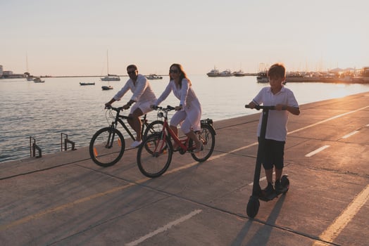 Happy family enjoying a beautiful morning by the sea together, parents riding a bike and their son riding an electric scooter. Selective focus photo
