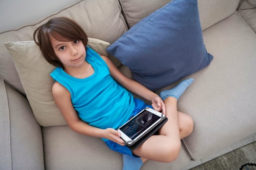 Little Arabian boy sitting on sofa and playing game on digital tablet photo
