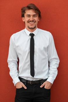 Portrait of startup businessman in a white shirt with a black tie standing in front of red wall outside photo