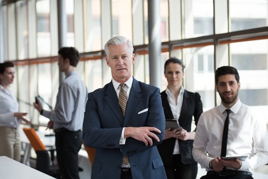 portrait of senior businessman as leader  with group of people in background as team photo