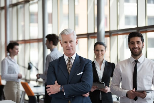 portrait of senior businessman as leader  with group of people in background as team photo