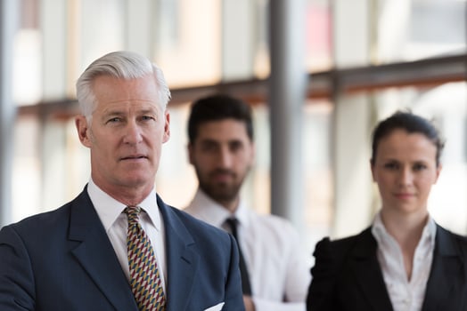 portrait of senior businessman as leader  with group of people in background as team photo