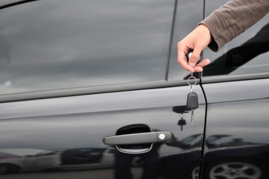 male hand holding car key with new black car in background photo