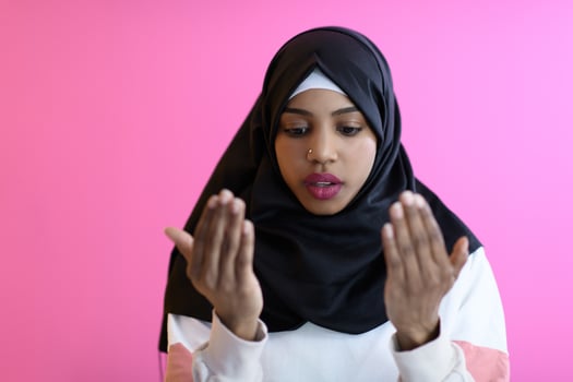 Modern African Muslim woman makes traditional prayer to God, keeps hands in praying gesture, wears traditional white clothes photo
