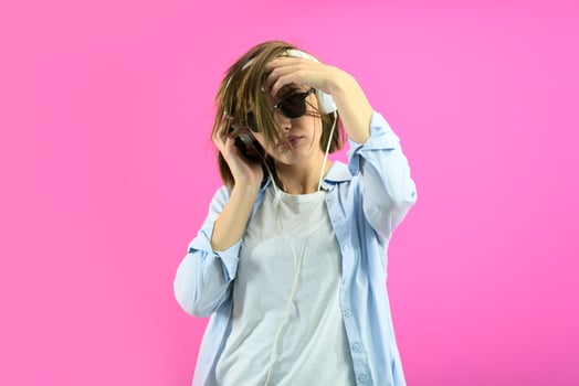 brunette lady in black glasses dancing and   listening music isolate on pink background photo