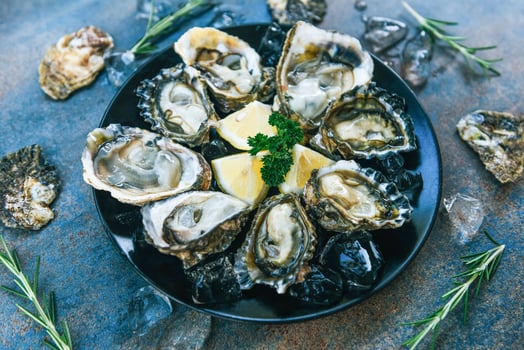 Fresh oysters seafood on a black plate background - Open oyster shell with herb spices lemon rosemary served table and ice healthy sea food raw oyster dinner in the restaurant gourmet food photo