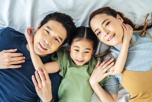 Top view of Happy Asian beautiful young mother, father and their daughter looking at camera and smiling while lying on bed head to head in bedroom photo