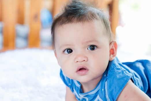 A beautiful 6 month old baby with big eyes lies on the bed. photo