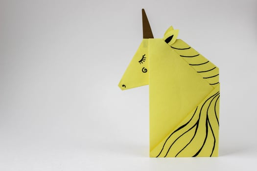 Yellow unicorn made in the origami technique on the right side of the photo on a white background. With place for your text.