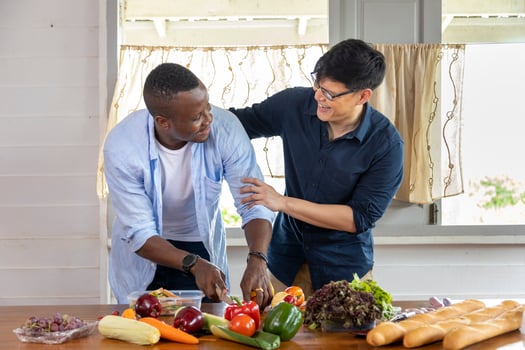 Diversity of LGBTQ gay couple between Asian and African ethnicity cooking together at home using organic vegetable to make salad and sandwich photo